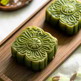 Two green cakes on a wooden board.
