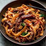 A bowl of noodles with meat and vegetables.